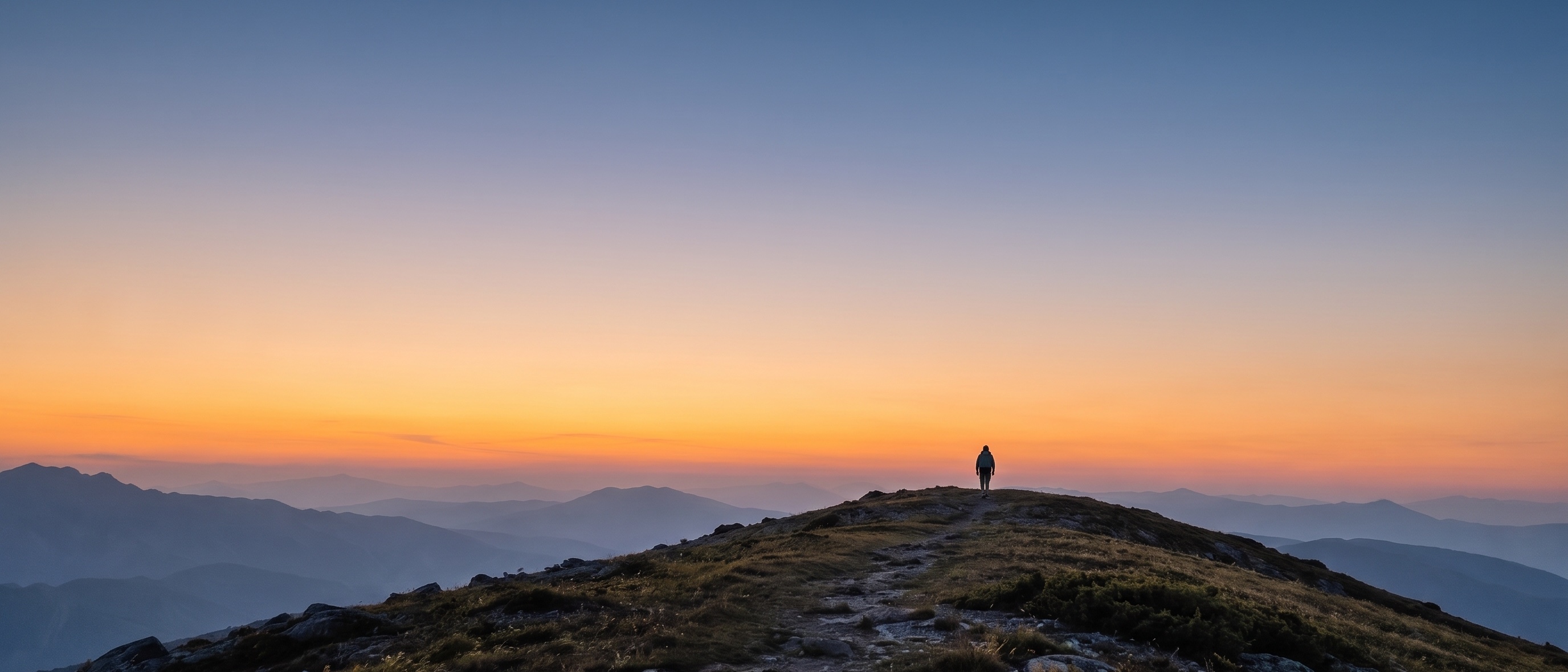 A lone figure walking along a distant mountain ridge at dusk
